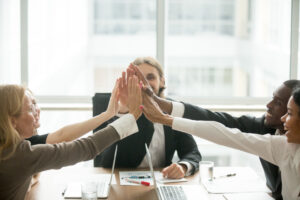 Vielfältiges Geschäftsteam gibt sich freudig High-Five während eines Meetings im Büro