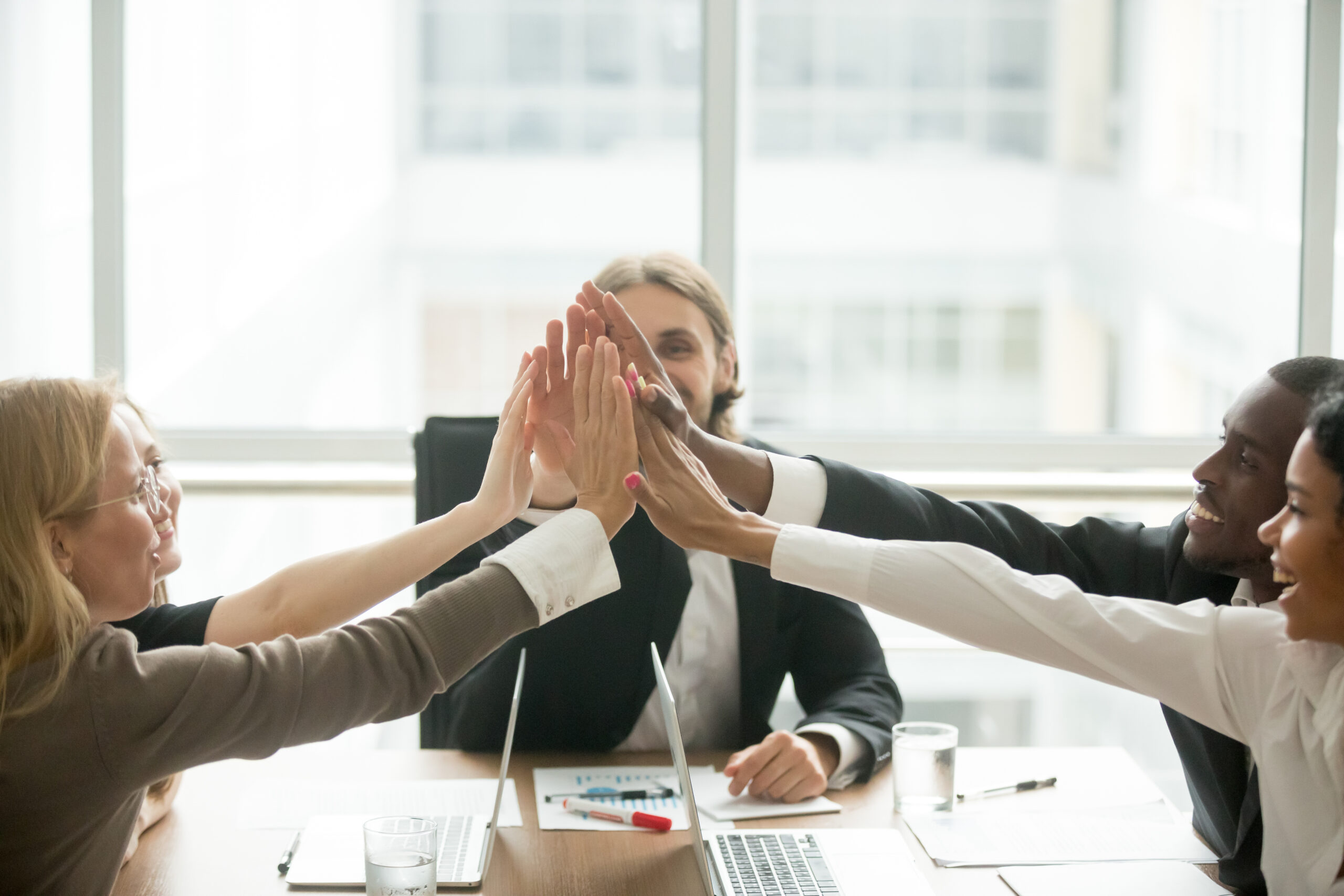Vielfältiges Geschäftsteam gibt sich freudig High-Five während eines Meetings im Büro
